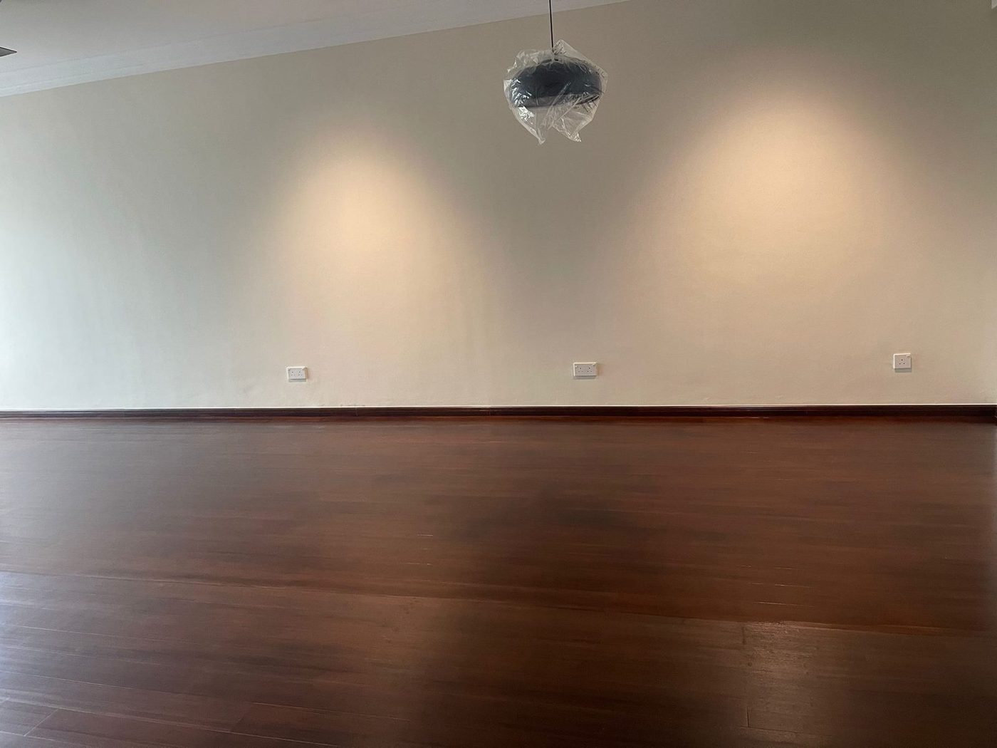 Wide view of a completed dark-strand bamboo floor in a Singapore residential room with downlight wash on the wall
